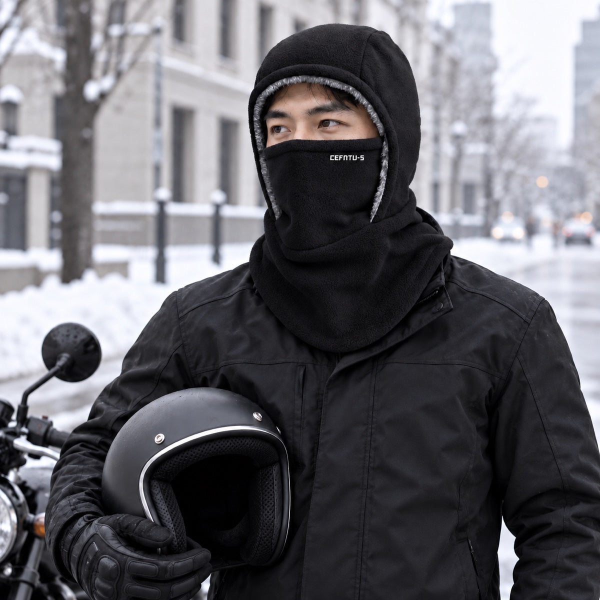 Motorbike rider wearing the black balaclava, helmet in hand, on a snowy city street